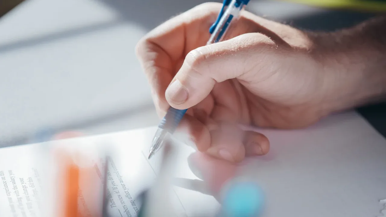 Skupiona dłoń trzymająca długopis podczas odręcznego pisania na jasnej kartce papieru